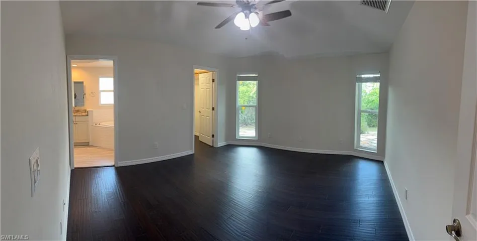 Empty room featuring dark wood-style floors, baseboards, a ceiling fan, and visible vents