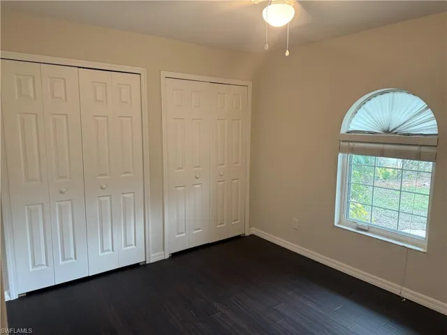 Unfurnished bedroom featuring multiple closets, baseboards, and dark wood finished floors