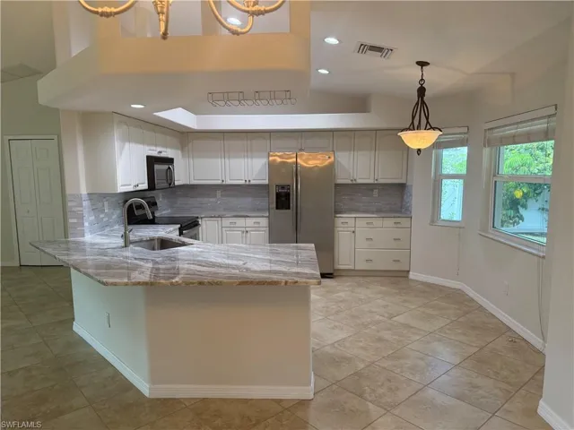 Kitchen featuring light stone countertops, appliances with stainless steel finishes, backsplash, and visible vents
