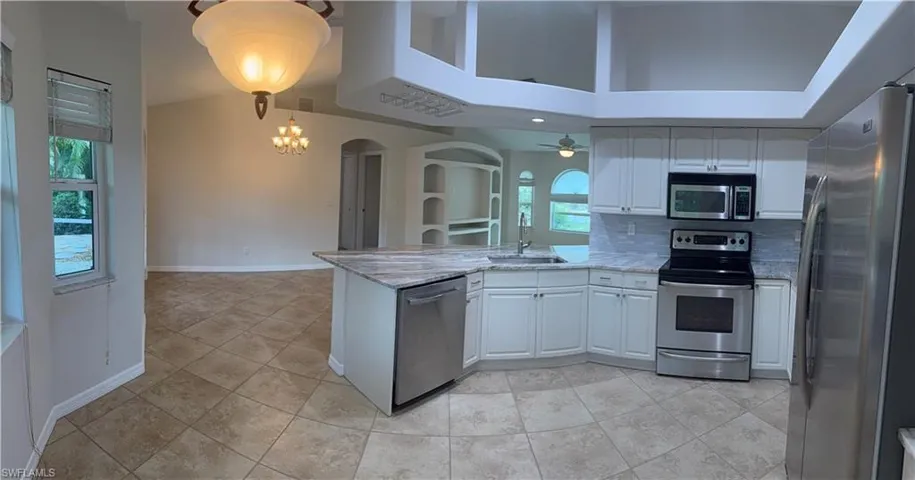 Kitchen featuring a peninsula, light stone countertops, stainless steel appliances, arched walkways, and a sink