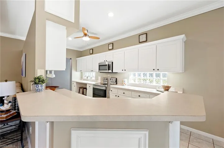 Kitchen featuring appliances with stainless steel finishes, crown molding, a peninsula, ceiling fan, and light countertops