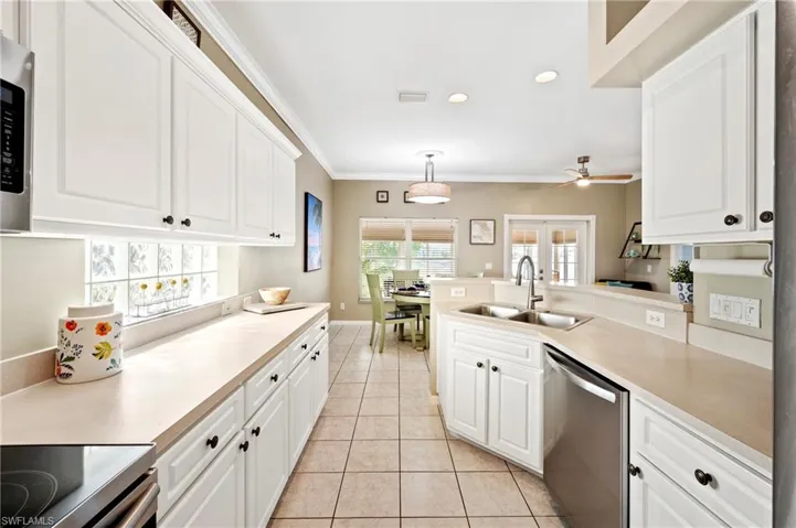 Kitchen featuring stainless steel appliances, light tile patterned floors, crown molding, white cabinets, and light countertops