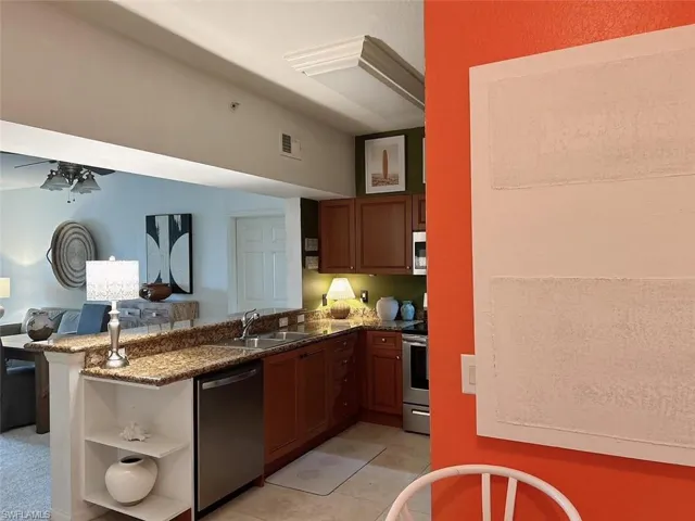 Kitchen featuring dark stone counters, kitchen peninsula, light tile floors, sink, and appliances with stainless steel finishes