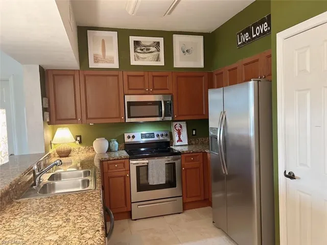 Kitchen with appliances with stainless steel finishes, sink, stone counters, and light tile flooring