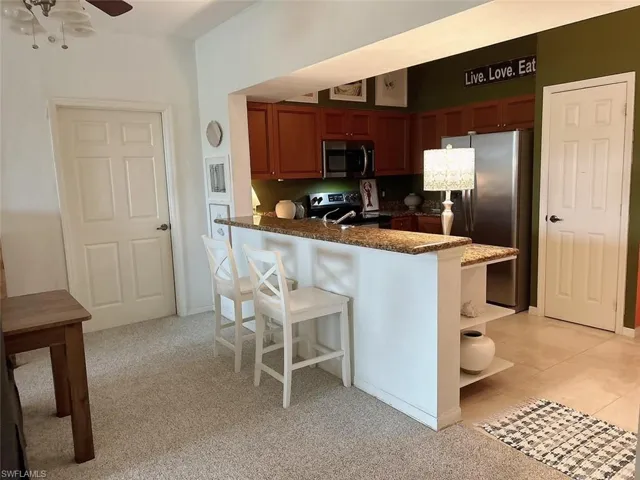 Kitchen featuring kitchen peninsula, ceiling fan, dark stone countertops, appliances with stainless steel finishes, and a breakfast bar