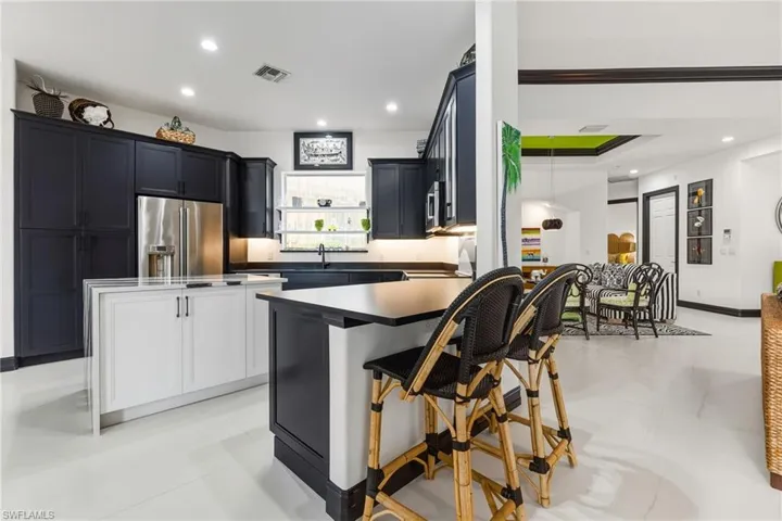Kitchen with dark cabinetry, stainless steel appliances, recessed lighting, a kitchen bar, and white cabinets