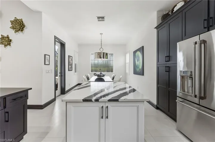 Kitchen with high end refrigerator, dark cabinets, light tile patterned flooring, pendant lighting, and a center island