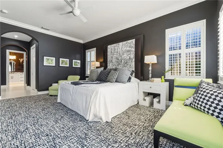 Bedroom with arched walkways, ornamental molding, a ceiling fan, and connected bathroom