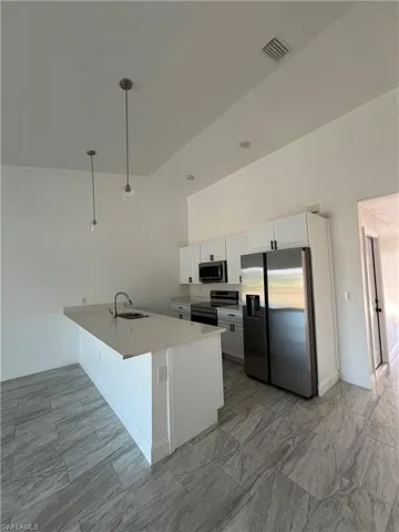 Kitchen featuring stainless steel appliances, white cabinets, a peninsula, a breakfast bar, and light stone counters