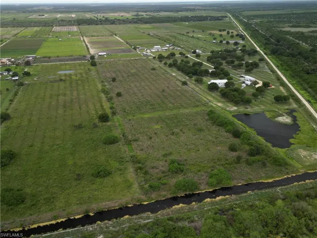 Expansive agricultural landscape featuring multiple cultivated fields, a substantial water canal, a pond, several structures, and mature trees