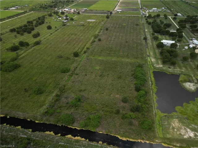Expansive agricultural land featuring a waterway, planted fields, a detention pond, and scattered trees