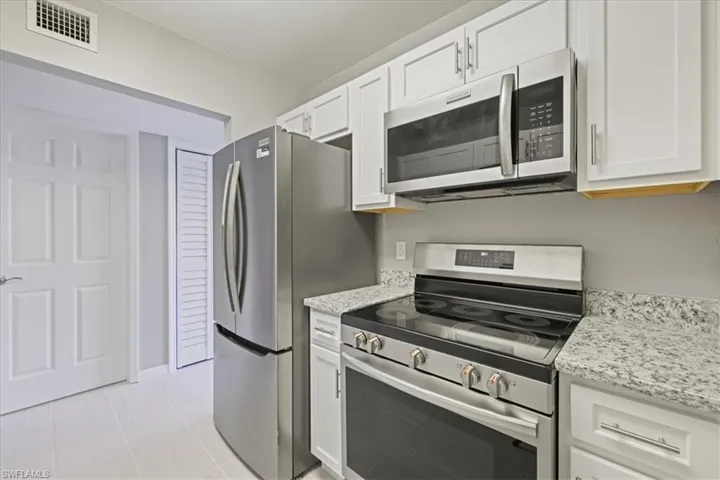 Kitchen with appliances with stainless steel finishes, white cabinetry, light tile patterned flooring, and light stone countertops