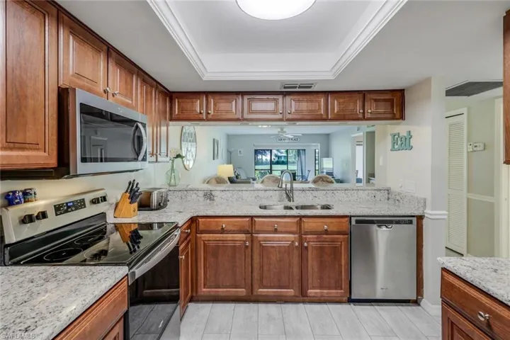 Kitchen featuring appliances with stainless steel finishes, a raised ceiling, wood tiled floors, light stone countertops, and brown cabinets