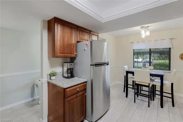 Kitchen featuring freestanding refrigerator, light wood finished floors, brown cabinets, and light stone countertops
