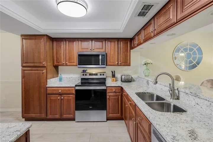 Kitchen featuring appliances with stainless steel finishes, a raised ceiling, light stone counters, light tile patterned floors, and brown cabinets