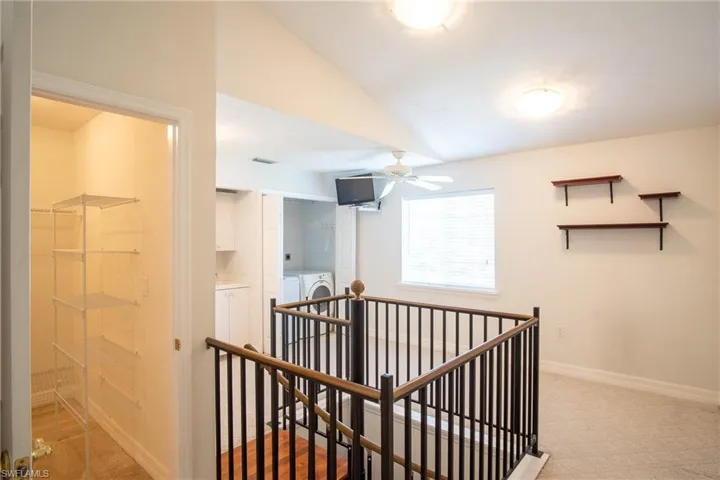Hallway with light colored carpet, independent washer and dryer, an upstairs landing, baseboards, and lofted ceiling