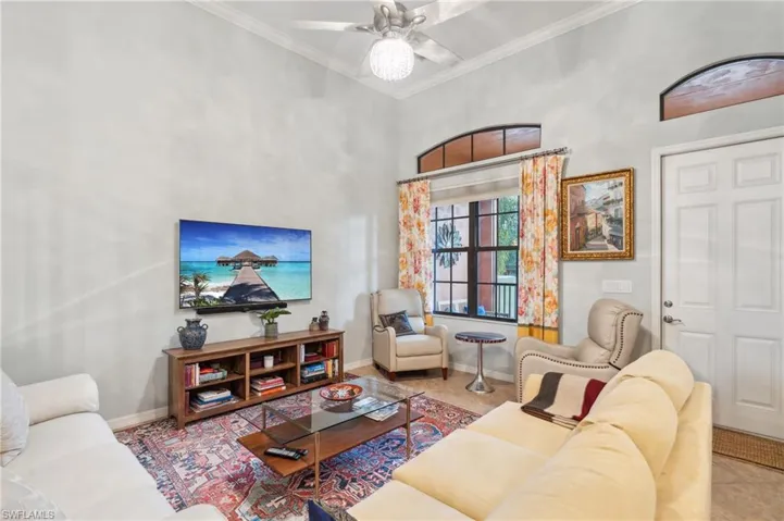 Living room with ceiling fan, ornamental molding, light tile patterned floors, and a towering ceiling