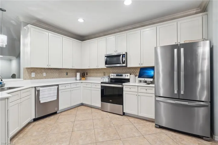 Kitchen with white cabinetry, backsplash, light tile patterned floors, stainless steel appliances, and sink