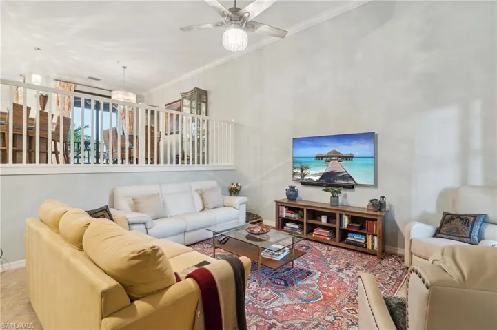 Living room with ornamental molding, ceiling fan with notable chandelier, and light tile patterned flooring