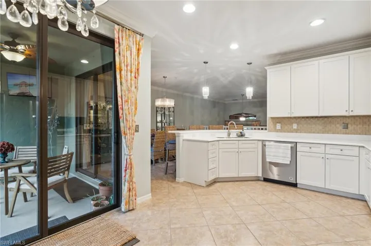 Kitchen featuring white cabinetry, stainless steel dishwasher, kitchen peninsula, pendant lighting, and ornamental molding