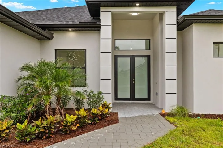 Entrance to property featuring professional landscaping, double impact glass door, and paved entry.