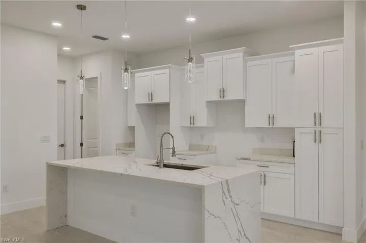 Kitchen featuring elegant light fixtures, waterfall island , 42" white cabinetry, and quartz countertops. Appliance included.