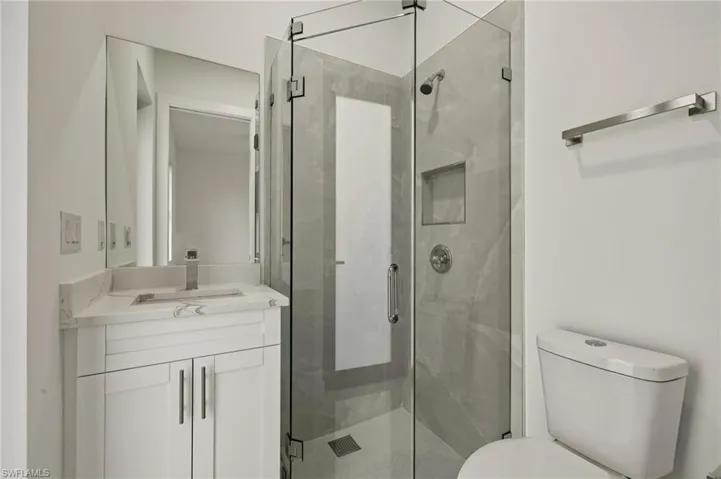 3rd bedroom bathroom featuring toilet, a tiled shower with frameless glass door, and vanity with quartz top. Glass door exit to the patio.
