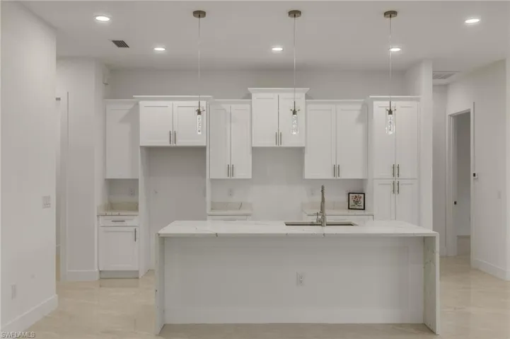 Kitchen featuring elegant light fixtures, waterfall island , 42" white cabinetry, and quartz countertops. Appliance included.