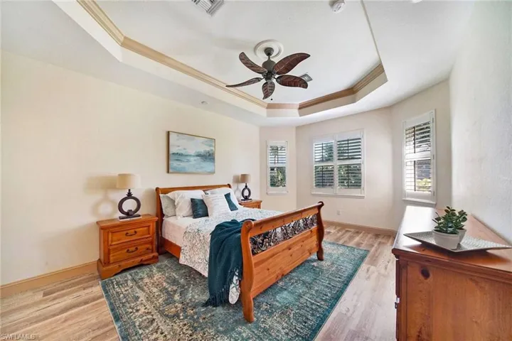 Bedroom with light hardwood / wood-style flooring, a raised ceiling, ceiling fan, and ornamental molding