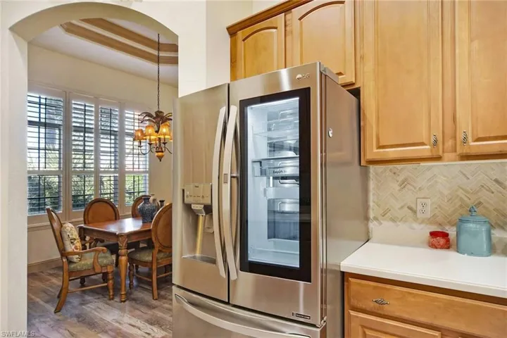 Kitchen featuring stainless steel fridge, backsplash, a raised ceiling, a chandelier, and hanging light fixtures