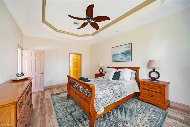 Bedroom featuring a tray ceiling, ceiling fan, ornamental molding, and light wood-type flooring