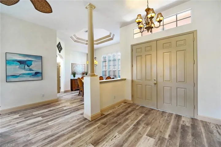 Foyer featuring ceiling fan with notable chandelier, a raised ceiling, wood-type flooring, and decorative columns