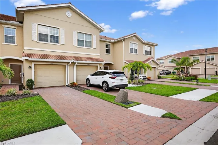 Townhome / multi-family property featuring driveway, an attached garage, stucco siding, a tile roof, and a front lawn