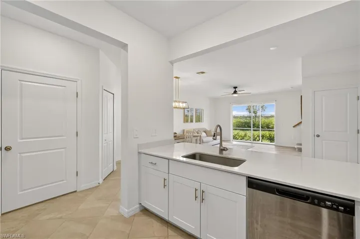 Kitchen with dishwasher, light countertops, white cabinets, open floor plan, and ceiling fan