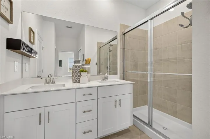 Full bath with a shower stall, double vanity, and tile patterned floors
