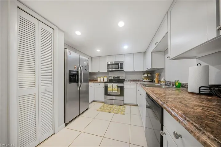 Kitchen with appliances with stainless steel finishes, light tile patterned floors, white cabinetry, recessed lighting, and dark countertops