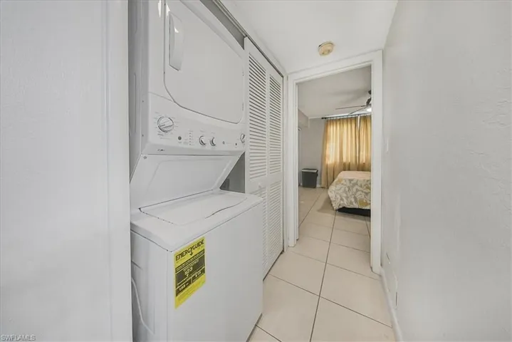 Laundry area featuring stacked washing machine and dryer, light tile patterned flooring, a textured wall, and a ceiling fan