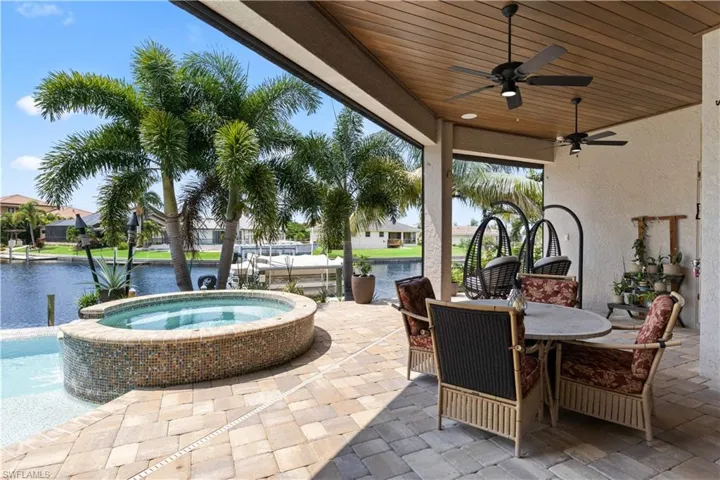 View of patio with a water view, ceiling fan, and an in ground hot tub