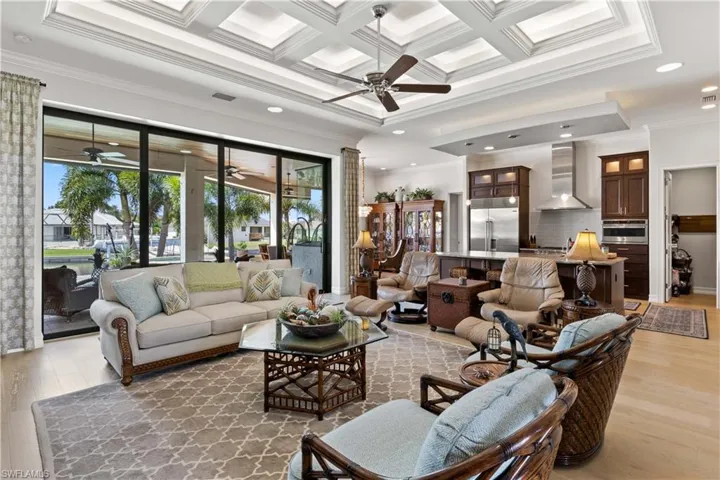 Living room with light hardwood / wood-style floors, coffered ceiling, beamed ceiling, ceiling fan, and ornamental molding