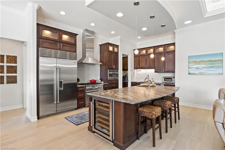 Kitchen featuring wine cooler, high end appliances, light stone countertops, pendant lighting, and wall chimney range hood