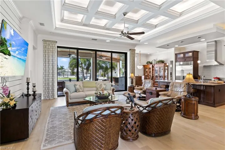 Living room with beamed ceiling, coffered ceiling, light hardwood / wood-style flooring, ornamental molding, and ceiling fan
