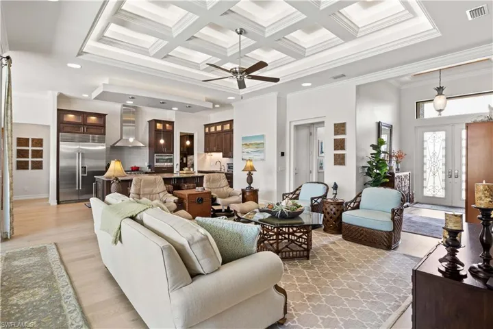 Living room featuring ceiling fan, beam ceiling, ornamental molding, light hardwood / wood-style flooring, and coffered ceiling