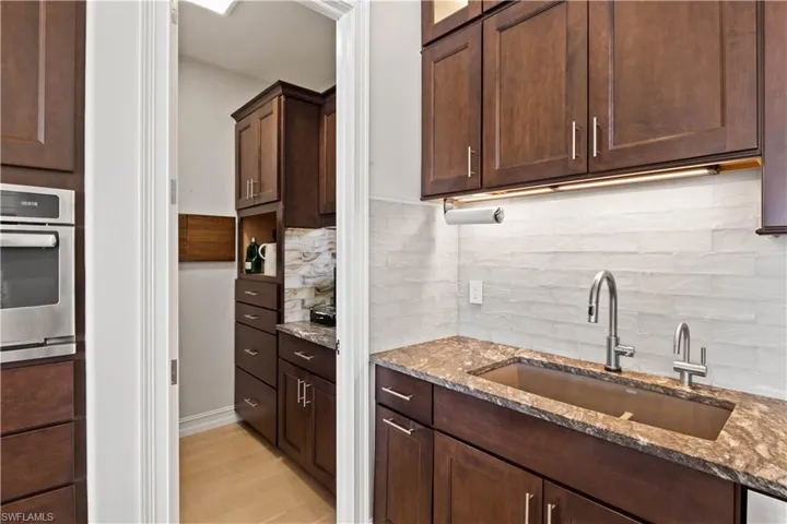 Kitchen featuring light stone countertops, stainless steel oven, tasteful backsplash, and sink
