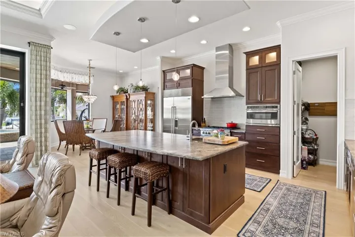Kitchen with pendant lighting, dark brown cabinets, an island with sink, wall chimney exhaust hood, and stainless steel appliances