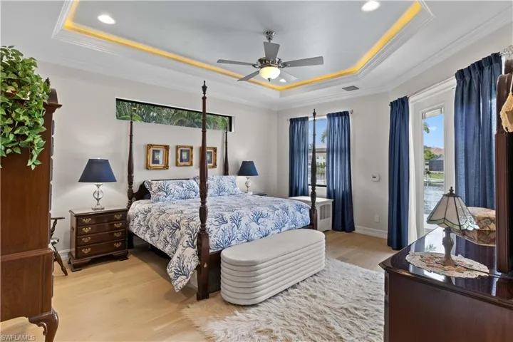 Bedroom with crown molding, light hardwood / wood-style floors, a tray ceiling, and ceiling fan