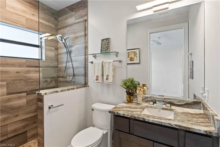 Bathroom featuring a tile shower, ceiling fan, vanity, and toilet