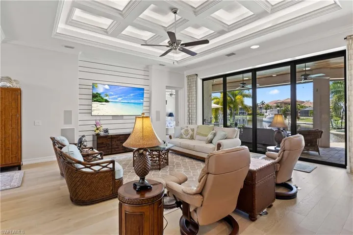 Living room featuring coffered ceiling, light wood-type flooring, crown molding, and plenty of natural light