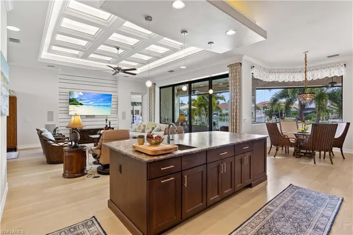 Kitchen with coffered ceiling, ceiling fan, an island with sink, and light hardwood / wood-style flooring