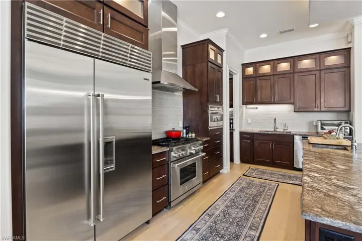 Kitchen with light wood-type flooring, tasteful backsplash, high end appliances, stone counters, and wall chimney range hood