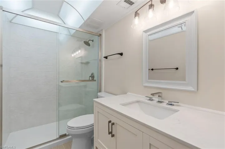 Bathroom featuring toilet, vanity, and a shower with door